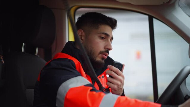 Young man doctor sitting and talking in to walkie-talkie in ambulance car.