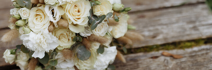 Banner wedding bouquet of white roses lies on old wooden boards. Wooden texture and green moss. Wedding rings.