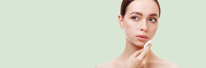 Banner portrait of an attractive young brunette woman with bare shoulders uses a Makeup Remover Pads, wipes her face on a white background. The concept of make-up, cosmetic procedures.