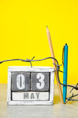 May 3 on calendar, barbed wire, ballpoint pen and pencil yellow background.Concept for Press...