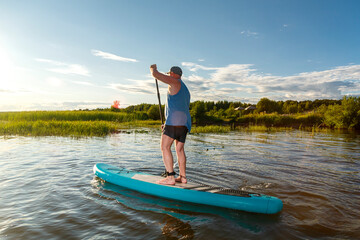 Fototapeta na wymiar a man in shorts stands with a paddle on a sup board at sunset in the water.