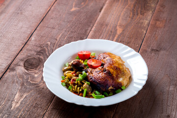 Pasta with vegetables and baked chicken leg with tomatoes sprinkled with green onions in a plate on the table.