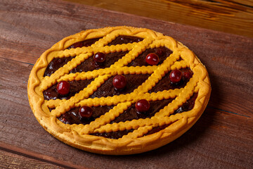 Cherry shortcrust pastry pie decorated with cherries on a wooden table.