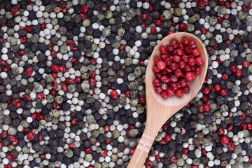 Red and black pepper peas in a wooden spoon on a white concrete, stone or slate background. view from above. close-up photo. pepper mixture