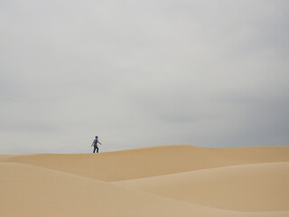 Fototapeta na wymiar silhouette of middle-aged man walking alone in the desert through sand barkhans in South American desert