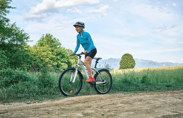 Fototapeta premium Cyclist Woman riding bike in helmets go in sports outdoors on sunny day a mountain in the forest. Silhouette female at sunset. Fresh air. Health care, authenticity, sense of balance and calmness. 