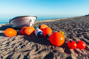 Orange Bojen und ein Fischerboot liegen auf einem Sandstrand am Ufer der Ostsee in der Sonne,...