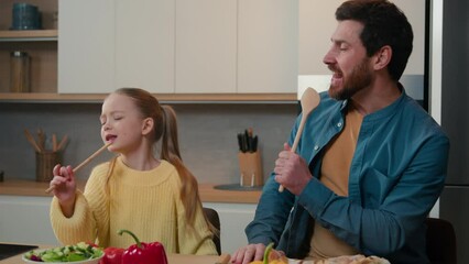 Funny Caucasian bearded father and cute little kid daughter singing song in kitchen funny cooking happy family dad with child girl holding spoon use like microphone sing enjoy cook having fun together