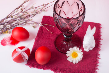 Easter still life with a white rabbit on a red background. A glass of wine and painted eggs - the concept of a bright Easter holiday