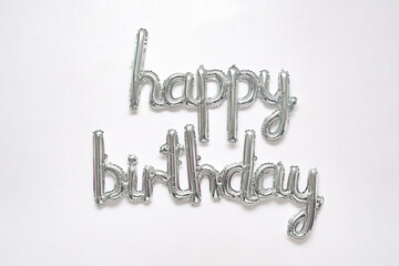 Silver happy birthday balloon lettering on a white wall. Foil letters isolated on horizontal background. Metallic greeting, party decor, event invite.
