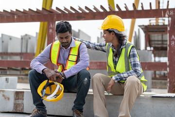 Asian Indian man worker feeling sad and upset while sitting at construction site. Female worker...