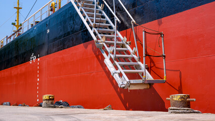 Perspective side view of white gangway accommodation ladder of red and black oil tanker while...
