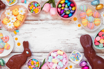 Easter candy frame. Top down view over a white wood background. Chocolate bunnies, candy eggs and an assortment of sweets. Copy space.