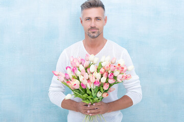 man with spring tulips smile isolated on blue background. photo of man with spring tulips.