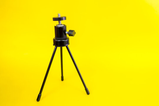 Black mini tripod with steel case and ballhead isolated on yellow background