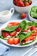 Spinach green crepes or pancakes with ricotta and strawberries on a plate for breakfast. Healthy...