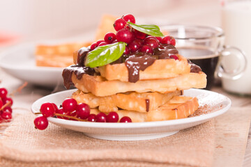 Waffle with red currant and chocolate topping on white dish.