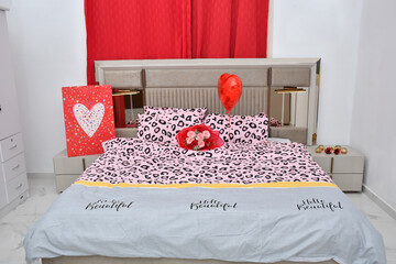 A bouquet of roses kept on a bed with a heart-shaped foil balloon and fancy bag kept a on a beautiful bed.