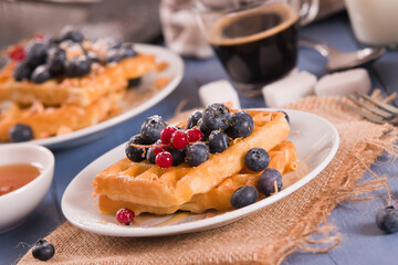 Waffles with red currant and blueberries on white dish.