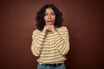 Young colombian curly hair woman isolated on brown background praying for luck, amazed and opening...