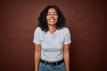 Young colombian curly hair woman isolated on brown background laughs and closes eyes, feels relaxed and happy.