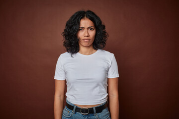 Young colombian curly hair woman isolated on brown background sad, serious face, feeling miserable and displeased.