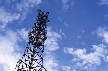 Wieża telefonii komórkowej na tle błękitnego nieba z chmurami.
