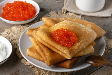 Stack of russian thin pancakes blini with red caviar on an old wooden table. Maslenitsa, traditional Russian blini