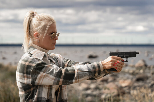 Beautiful girl in sunglasses by the sea with a 9mm pistol in her hands.