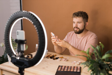 Man talking on cosmetics holding a makeup tools while recording his video. Guy making video for his blog on cosmetic product