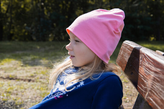 Child girl in a hat sits on a wooden bench on the street - Powered by Adobe
