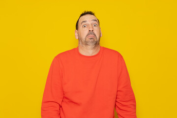 Obraz premium Bearded latino man wearing a red sweater with expression of doubt and confusion shrugging shoulders isolated over yellow background.