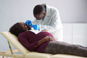 Naklejka na ściany i meble Dentist Treating Teeth Of Young Pregnant Woman Patient Lying