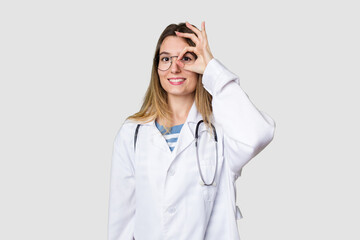 Compassionate female physician with a stethoscope around her neck, ready to diagnose and care for her patients in her signature white coat excited keeping ok gesture on eye.