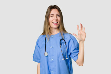 Young female nurse in uniform with stethoscope, symbol of care and dedication to patients laughs out loudly keeping hand on chest.
