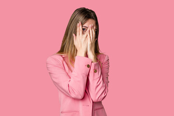 Young blonde posing for a portrait isolated, exuding natural beauty and radiance blink through fingers frightened and nervous.