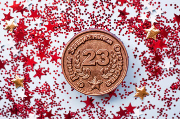 Greeting card for the Defender of the Fatherland Day. The inscription is in Russian. White, gold, red stars, an iron medal with the date February 23 on a blue background. The holiday is February 23.