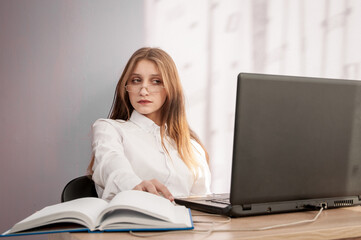 The girl is sitting at the table and looking at the laptop.