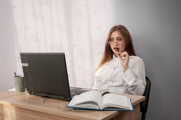 The girl is sitting at the table and looking at the laptop.