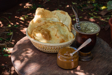 mate argentino con torta frita y dulce de leche sobre una pequeña mesa de madera rústica,