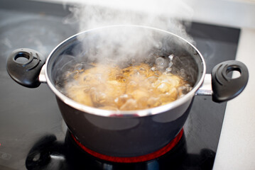Varias patatas cociéndose en una olla con agua hirviendo. Concepto de preparar una receta con...