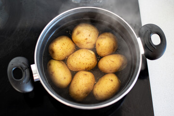 Varias patatas cociéndose en una olla con agua hirviendo. Concepto de preparar una receta con...
