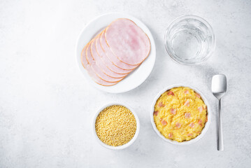 Cheesy millet with ham slices in a baking bowl