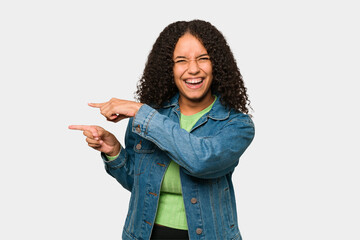 Young african american curly woman isolated excited pointing with forefingers away.