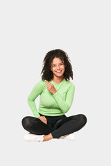 Young african american curly woman sitting on the floor isolated
