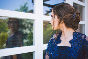 Beautiful girl in glamorous dress looking at herself in the window glass