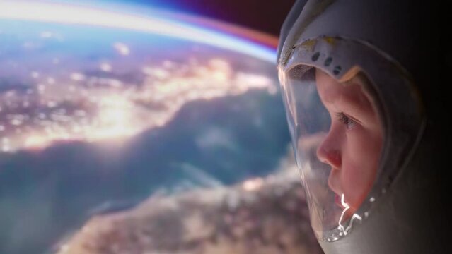 Little boy Astronau in space helmet looks at planet earth from spaceship enjoying sunrise over earth in space. Space day. Child dreams of becoming an astronaut.