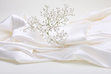 White beige pearl wave fabric silk and Gypsophila flower twig. Abstract texture horizontal copy space background.