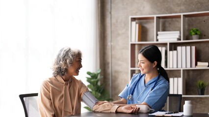 Nurse measuring blood pressure of senior woman. Smiling to each other. Doctor checking elderly woman's blood pressure