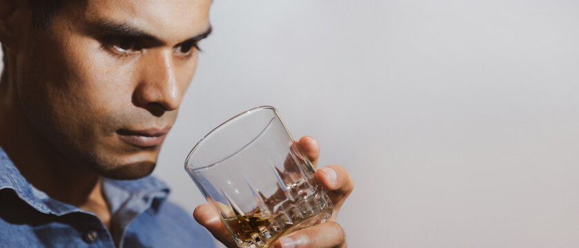 hombre joven triste y mirando con bebida en su mano en un fondo gris y espacio para texto, concepto de problemas con las bebidas alcoh&oacute;licas, depresi&oacute;n, alcoholismo. 